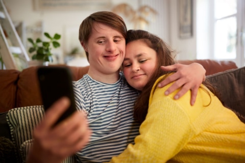 zwei junge Menschen mit Down-Syndrom machen ein Selfie auf der Couch